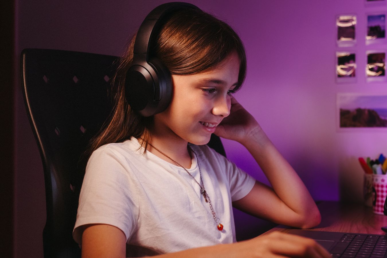 Adolescente sonriente usando laptop y audífonos desde su recámara